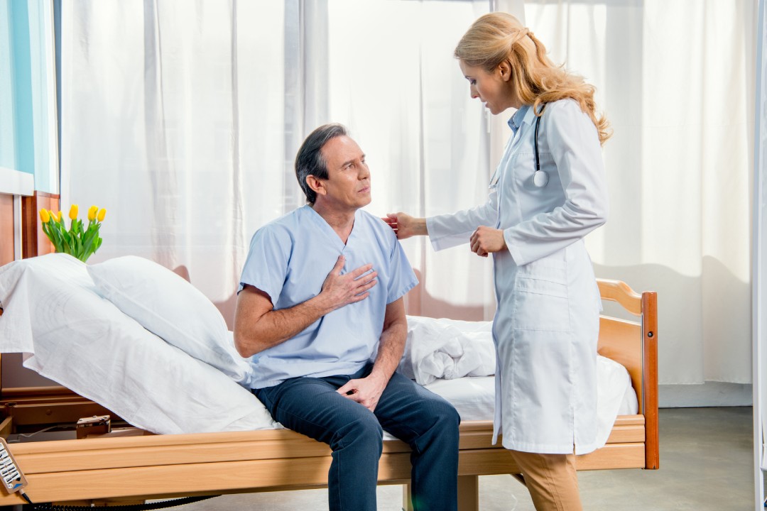 Middle aged man with chest pain and doctor standing near him in hospital