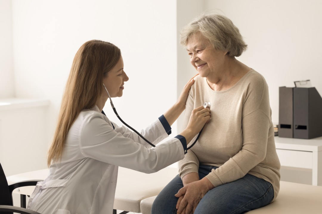 Cardiologist in coat examines older woman in clinic, listen to heartbeat with stethoscope during patient visit. Elderly woman passes heart check-up in hospital. Citizen healthcare services, cardiology