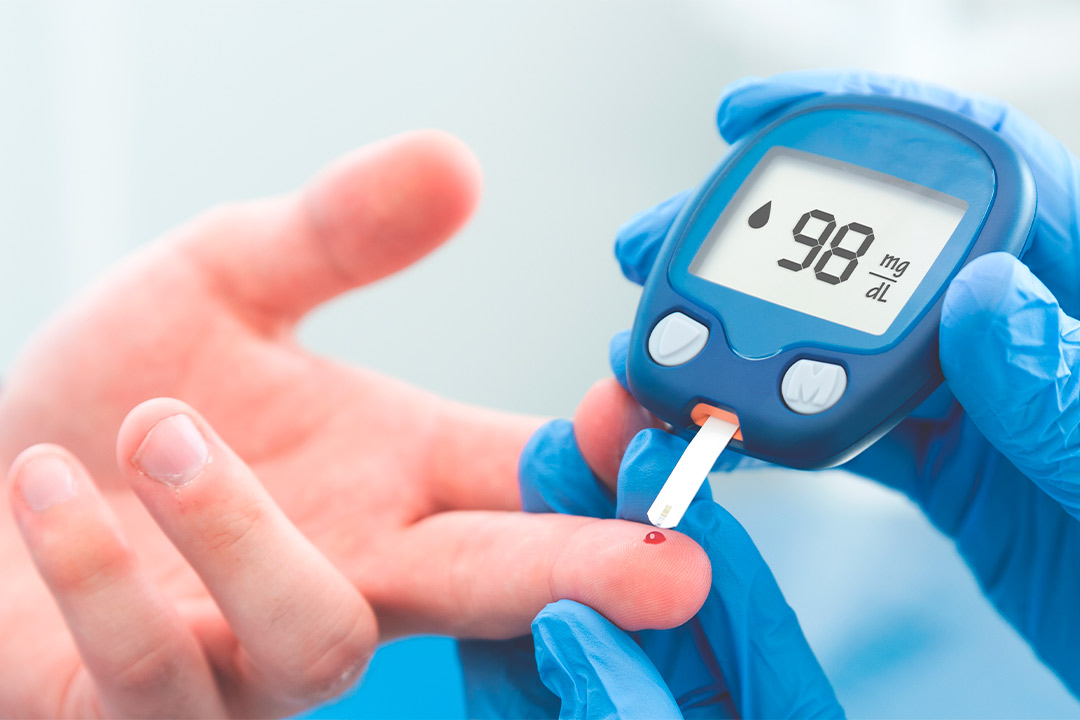 A person wearing blue gloves holds a blood glucose meter, emphasizing the importance of men's health monitoring.