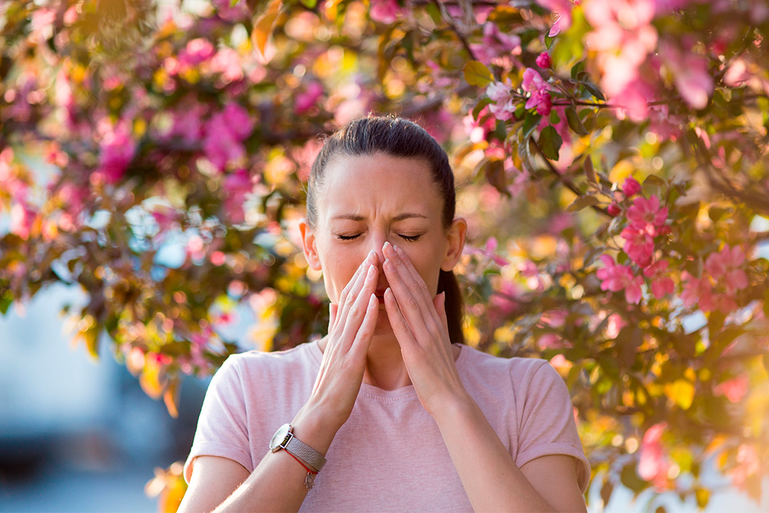 A woman blows her nose in front of a tree, highlighting asthma triggers during South Texas summers.