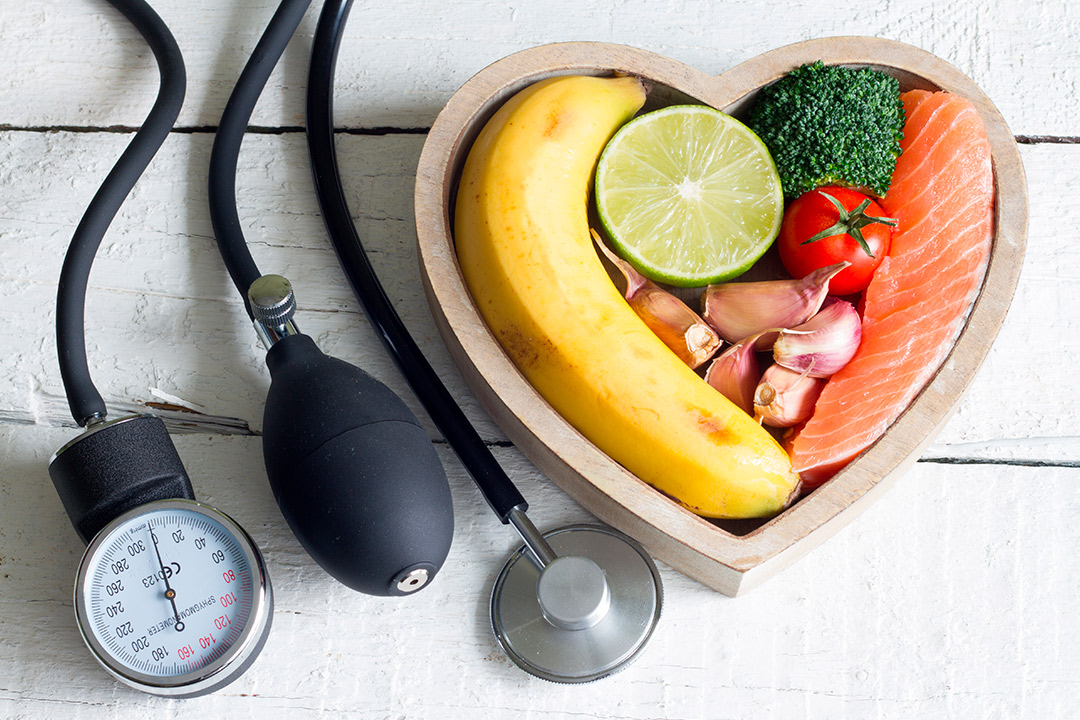 Heart-shaped bowl with a stethoscope, fruits, vegetables, and a banana, symbolizing health and diabetes management.