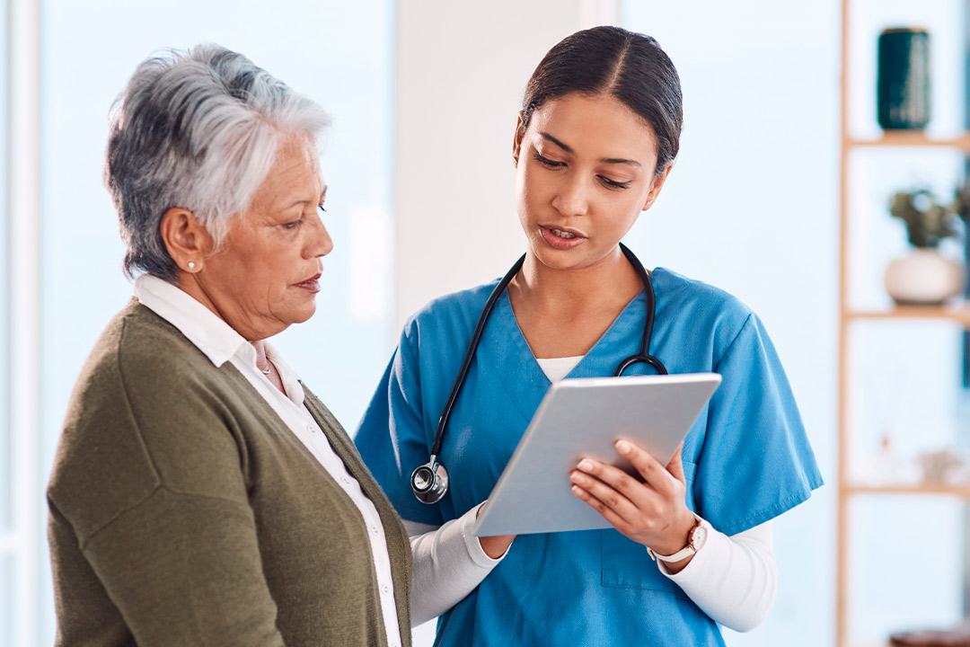An elderly woman and a nurse examine a tablet together, emphasizing the importance of skilled nursing in chronic illness care.