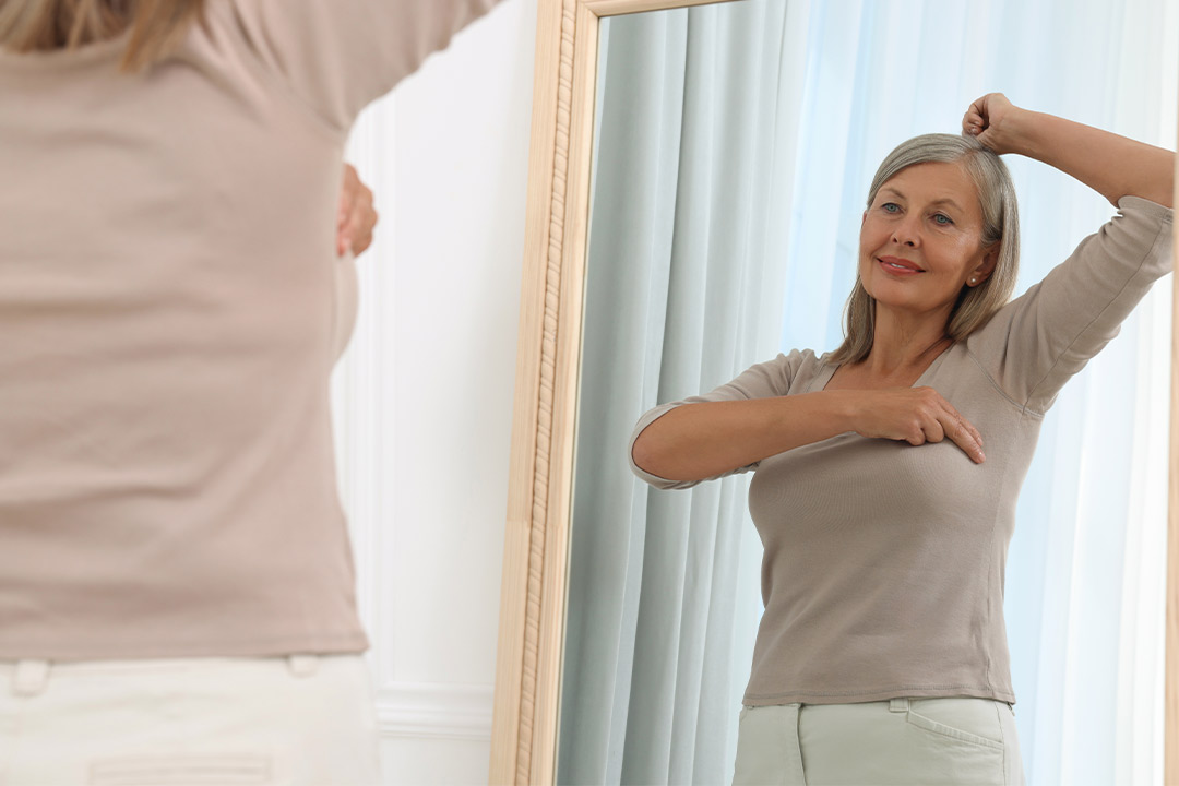A woman examines her reflection in a mirror, representing the importance of self-care in cancer prevention efforts.