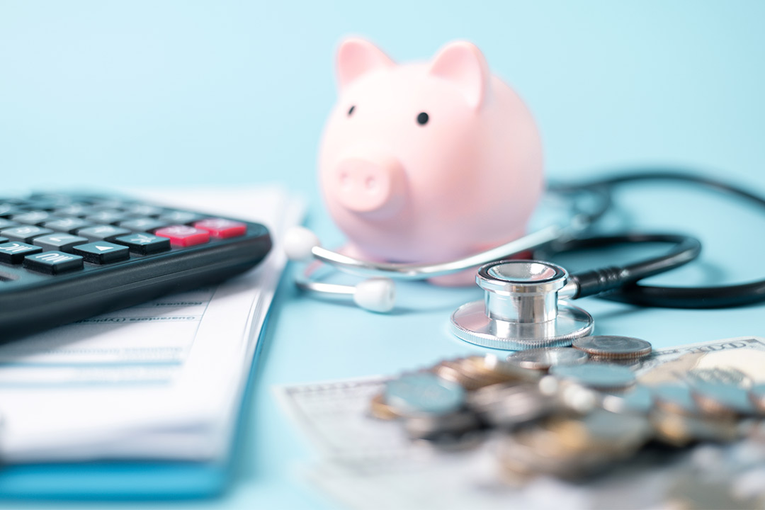 Image of a piggy bank, stethoscope, calculator, and money on blue, illustrating understanding insurance for routine healthcare.