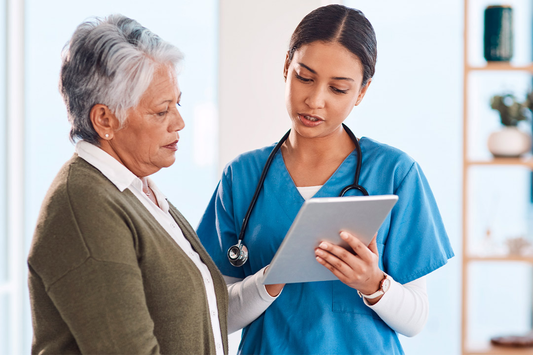 An older woman and a nurse examine a tablet, focusing on understanding insurance for routine medical appointments.